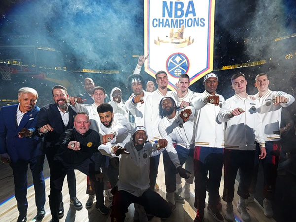 Para pemain dan jajaran pelatih Denver Nuggets berpose dengan cincin juara, sementara banner kejuaraan dikerek ke langit-langit. (Foto: NBA)