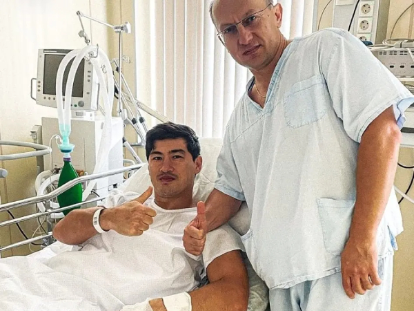 Dmitry Bivol (kiri) berpose di ranjang rumah sakit setelah menjalani operasi punggung. (Foto: Fight TV)