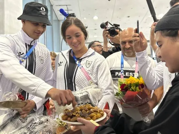 Atlet Olimpiade Palestina, Yazan Al Bawab (kiri) dan Valerie Tarazi, mencicipi buah kurma yang diberikan seorang suporter saat tiba di Bandara Paris Charles de Gaulle, di Rossy, sebelah utara Paris pada Kamis (25/7). (Foto: AP)