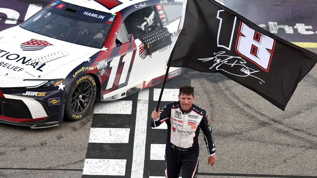 Denny Hamlin mengibarkan bendera hitam bernomor 18 yang identik dengan mendiang rekan setimnya, Kyle Busch. (Foto: AP)