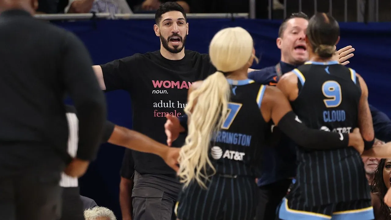 Enes Kanter Freedom (kiri) berada di kursi penonton di tepi lapangan dan mengenakan kaus hitam bertuliskan "WOMAN noun. adult human female." (Foto: AP)